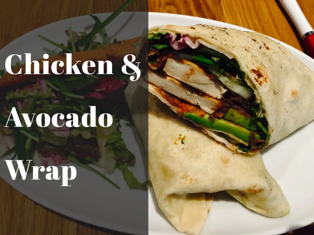A gourmet chicken avocado wrap sliced in half on a rustic wooden board, showing layers of grilled chicken, ripe avocado slices, and vibrant red peppers.