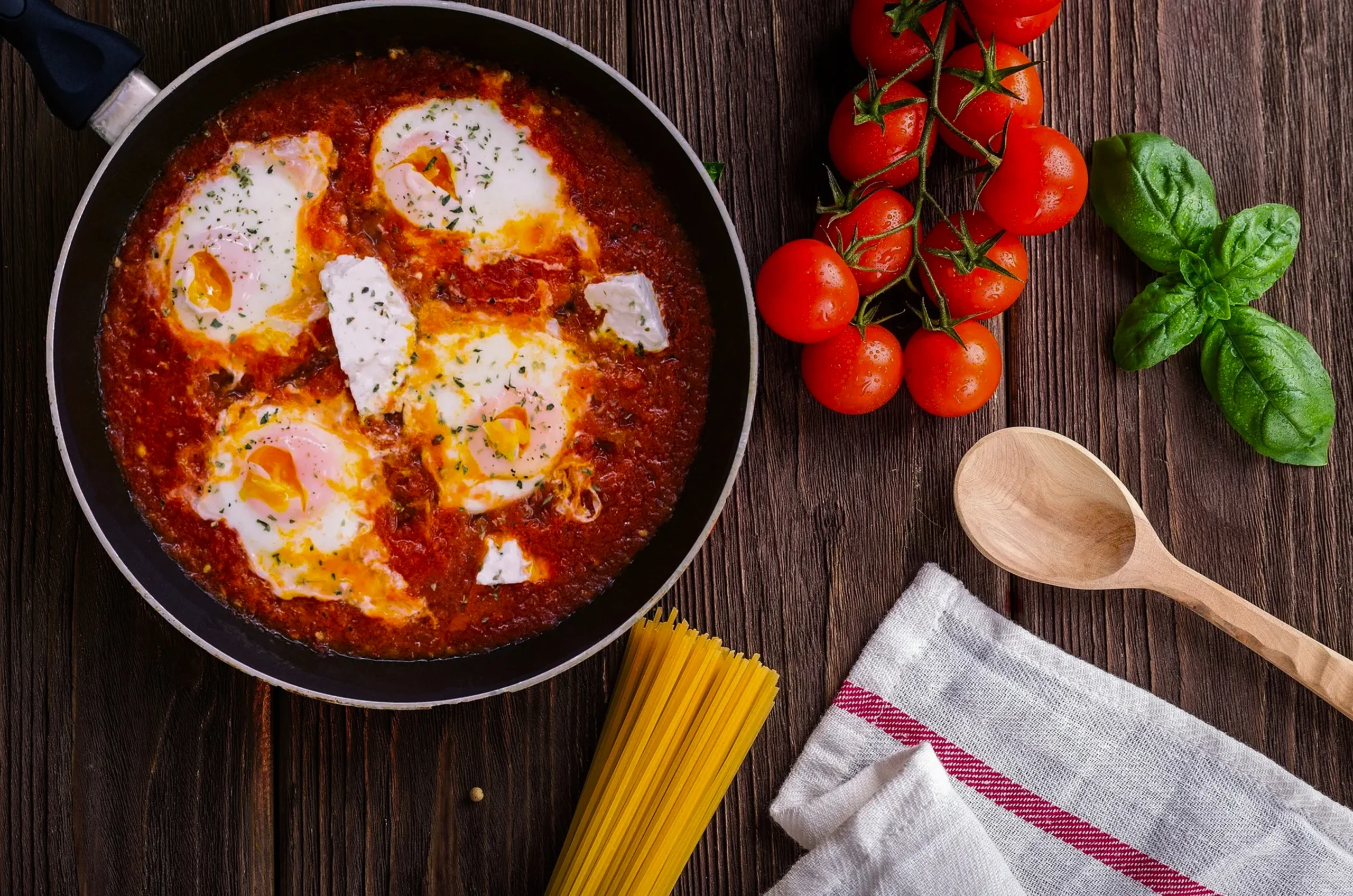 Close-up of a runny egg yolk in a bubbling Shakshuka base with crumbled feta cheese and a side of crusty sourdough.