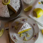 A thick slice of moist lemon loaf cake on a white plate, showing the saturated "drizzle" layer near the top crust.
