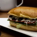 Close-up of pan-fried halloumi slices with a thick layer of basil pesto and balsamic glaze on a ciabatta roll.