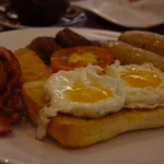 Traditional British fry-up breakfast plate served with buttered toast and a cup of English breakfast tea.