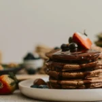 Thick buttermilk pancakes dusted with powdered sugar and garnished with edible flowers on a ceramic plate.