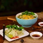 Close-up of a spoonful of golden chicken broth with rotisserie chicken, carrots, celery, and spiral noodles.