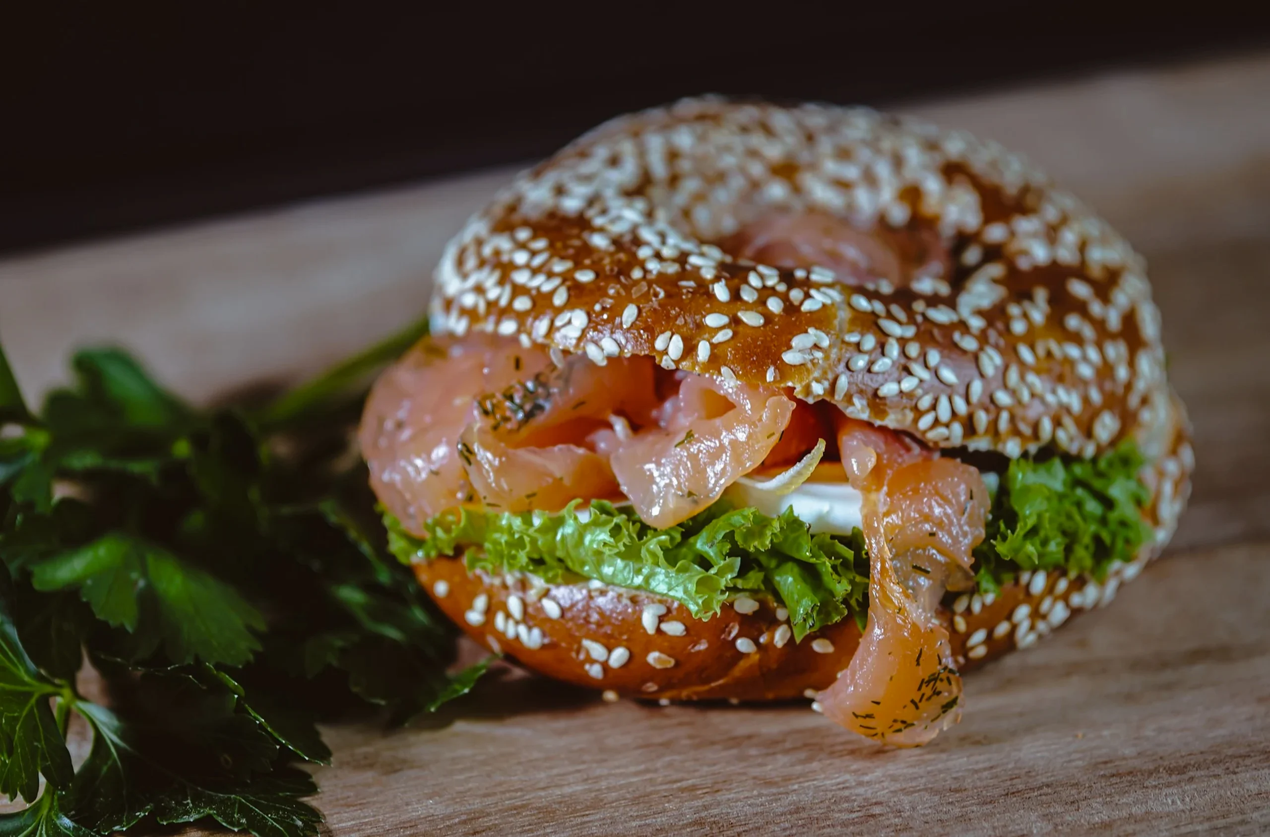 Close-up of a New York style sesame bagel with layers of Scottish smoked salmon, red onion slices, and a squeeze of lemon.