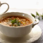 Close-up of a spoonful of chunky vegetable minestrone with a sprinkle of parmesan cheese and crusty bread.
