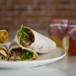 Close-up of a hearty breakfast wrap with black pudding, fried potatoes, and melted cheddar cheese in a flour tortilla.