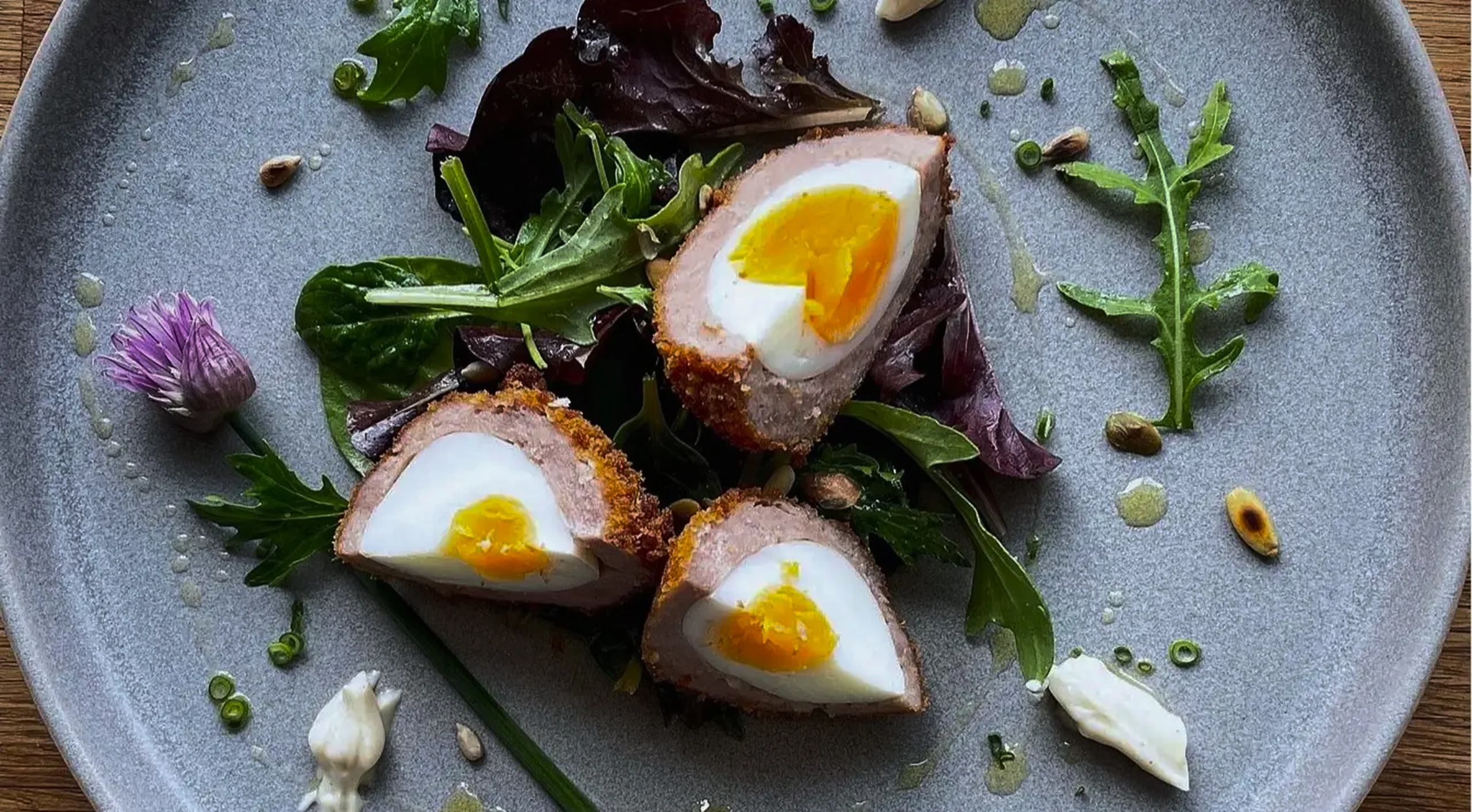 A soft-boiled Scotch egg sliced in half showing a jammy golden yolk, crispy sausage meat coating, and panko breadcrumbs.