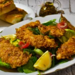 Close-up of golden-brown fried chicken strips on a bed of fresh romaine lettuce with a drizzle of Caesar sauce.