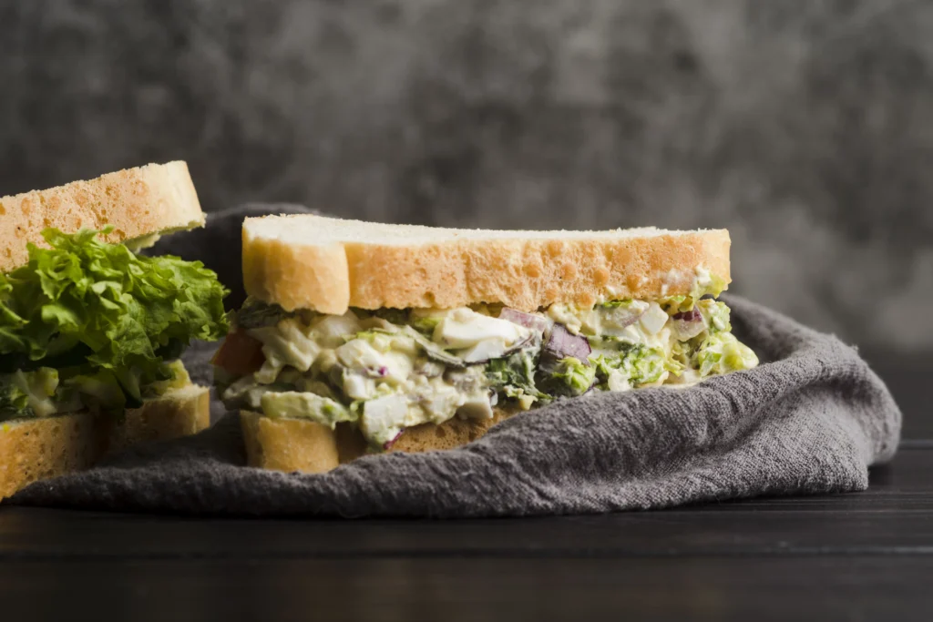 A close-up, high-angle shot of two halves of a Japanese egg salad sandwich (Tamago Sando) served on a wooden cutting board.
