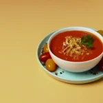 A bowl of velvety orange-red tomato soup garnished with a drizzle of olive oil and golden sourdough croutons.