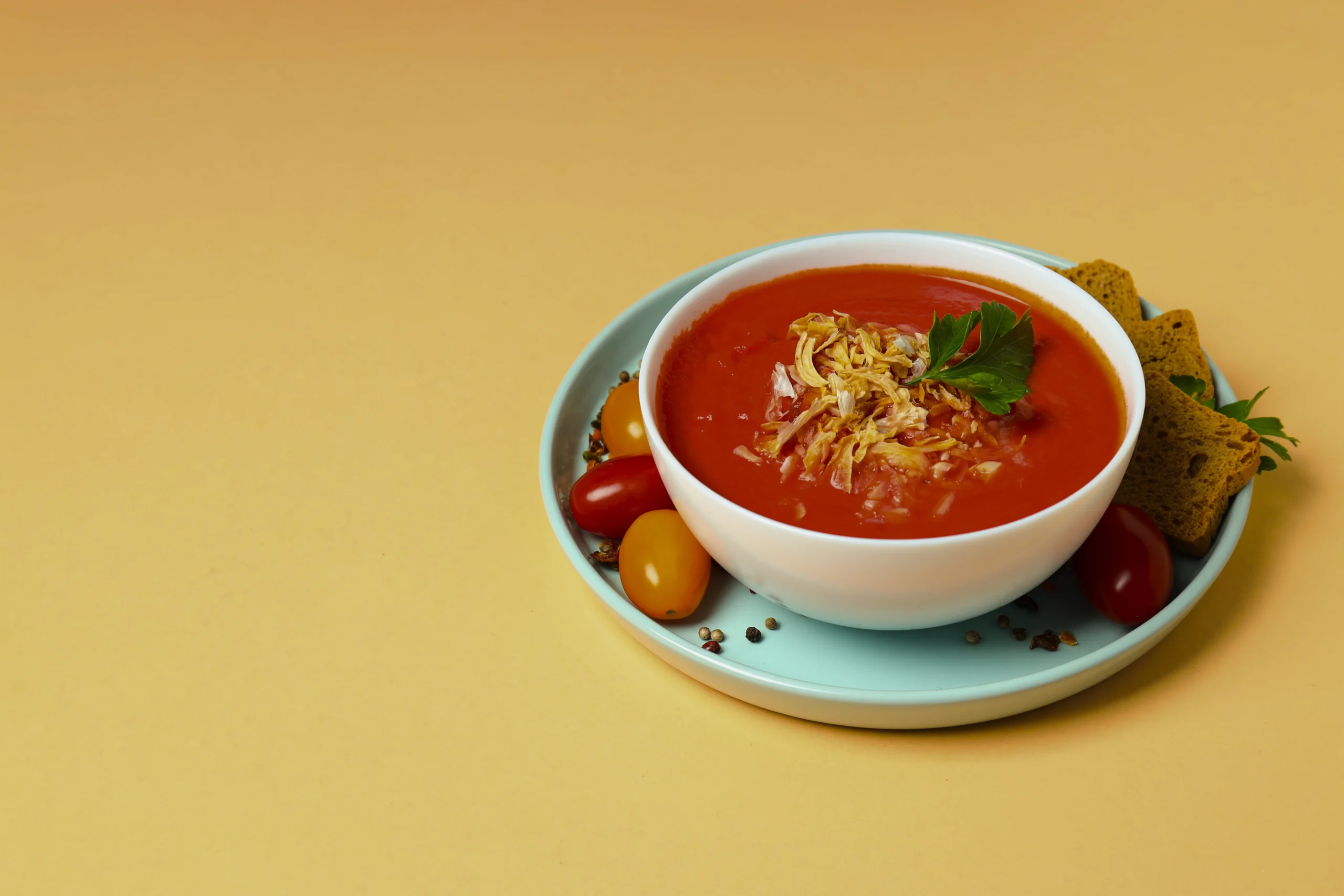 A bowl of velvety orange-red tomato soup garnished with a drizzle of olive oil and golden sourdough croutons.