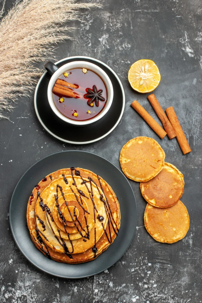 A stack of thin, golden-brown British pancakes served with a fresh lemon wedge and sugar dusting.