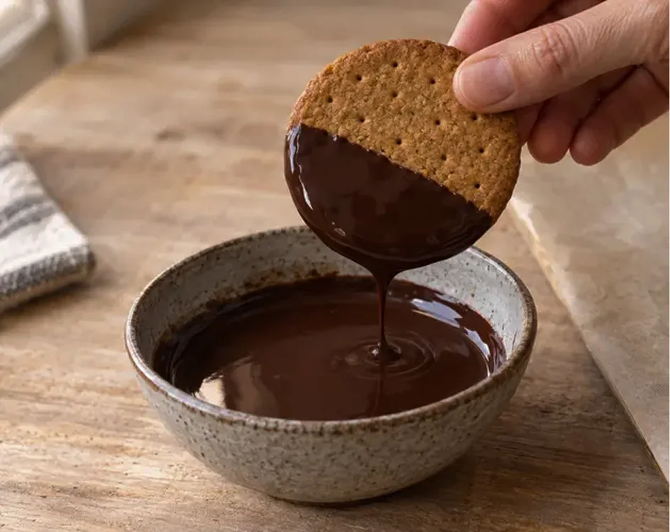 Dipping a digestive biscuit halfway into melted dark chocolate