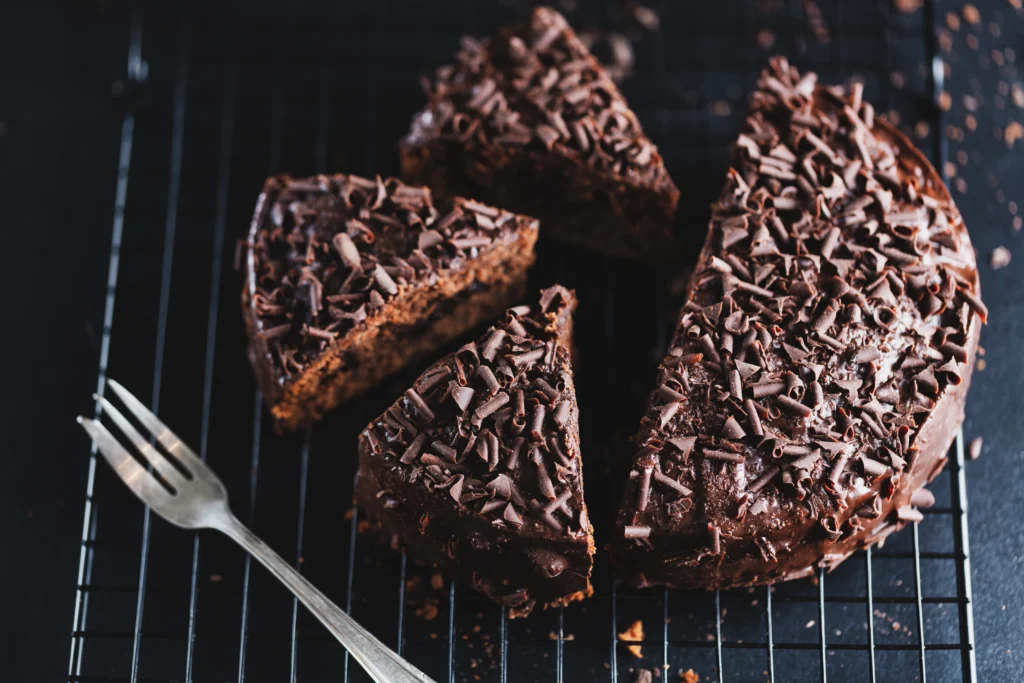 Slices of moist chocolate fudge cake with layers of rich chocolate ganache frosting and chocolate shavings on a cake stand.