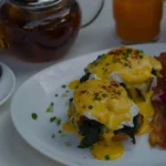 Close-up of traditional Eggs Benedict with Canadian bacon and runny egg yolk, showing how to layer the brunch classic.