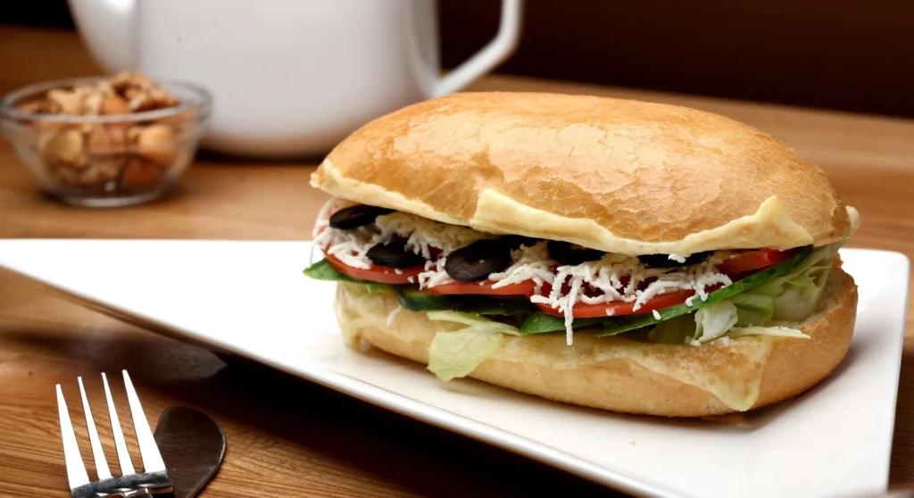 Close-up of a grilled Halloumi sandwich with visible char marks on the cheese, oozing with a rich pine nut pesto and nestled between layers of roasted red peppers and arugula.