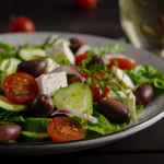 A vibrant bowl of traditional Horiatiki Greek salad showing juicy tomatoes, crisp bell peppers, and dried oregano.