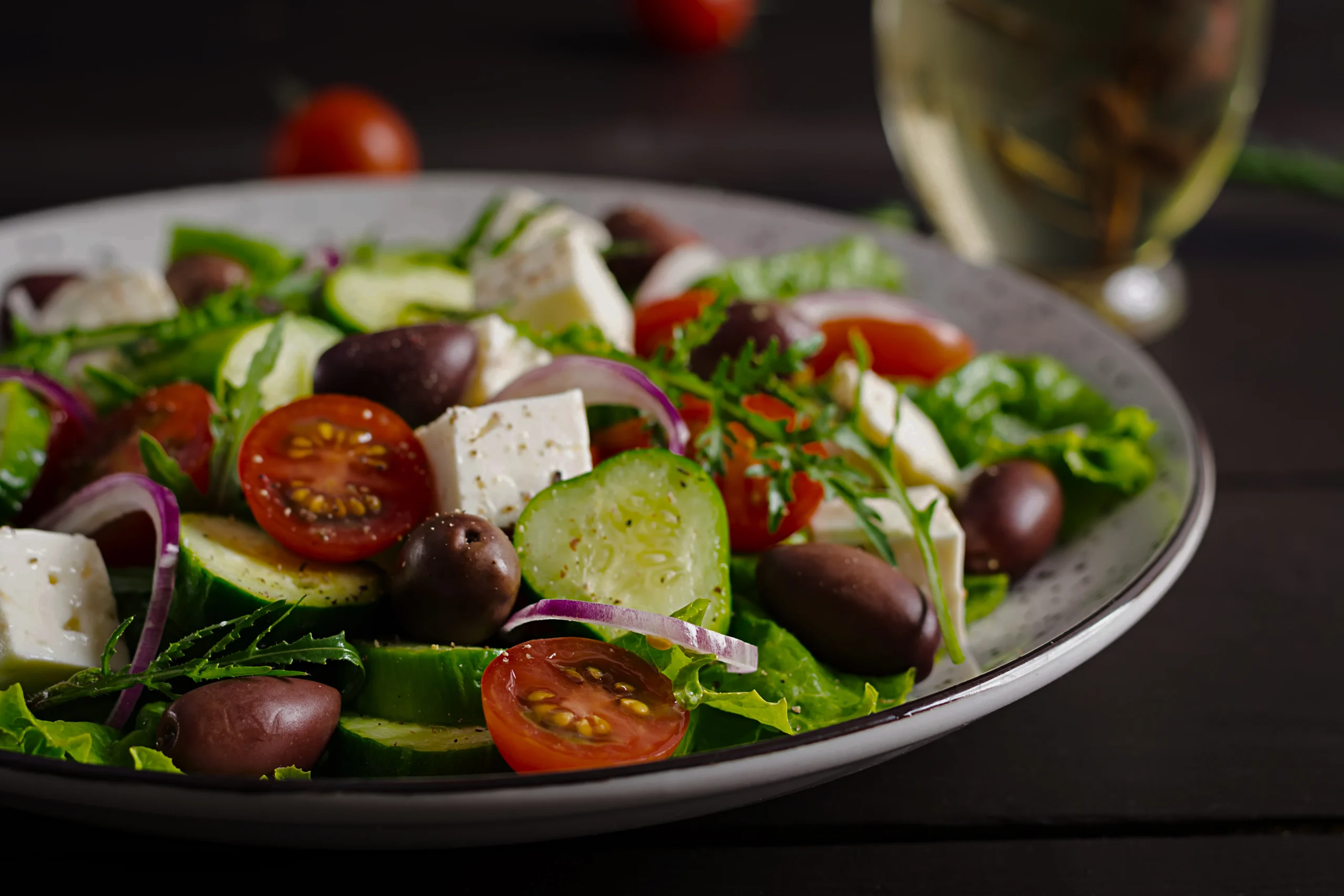 A vibrant bowl of traditional Horiatiki Greek salad showing juicy tomatoes, crisp bell peppers, and dried oregano.