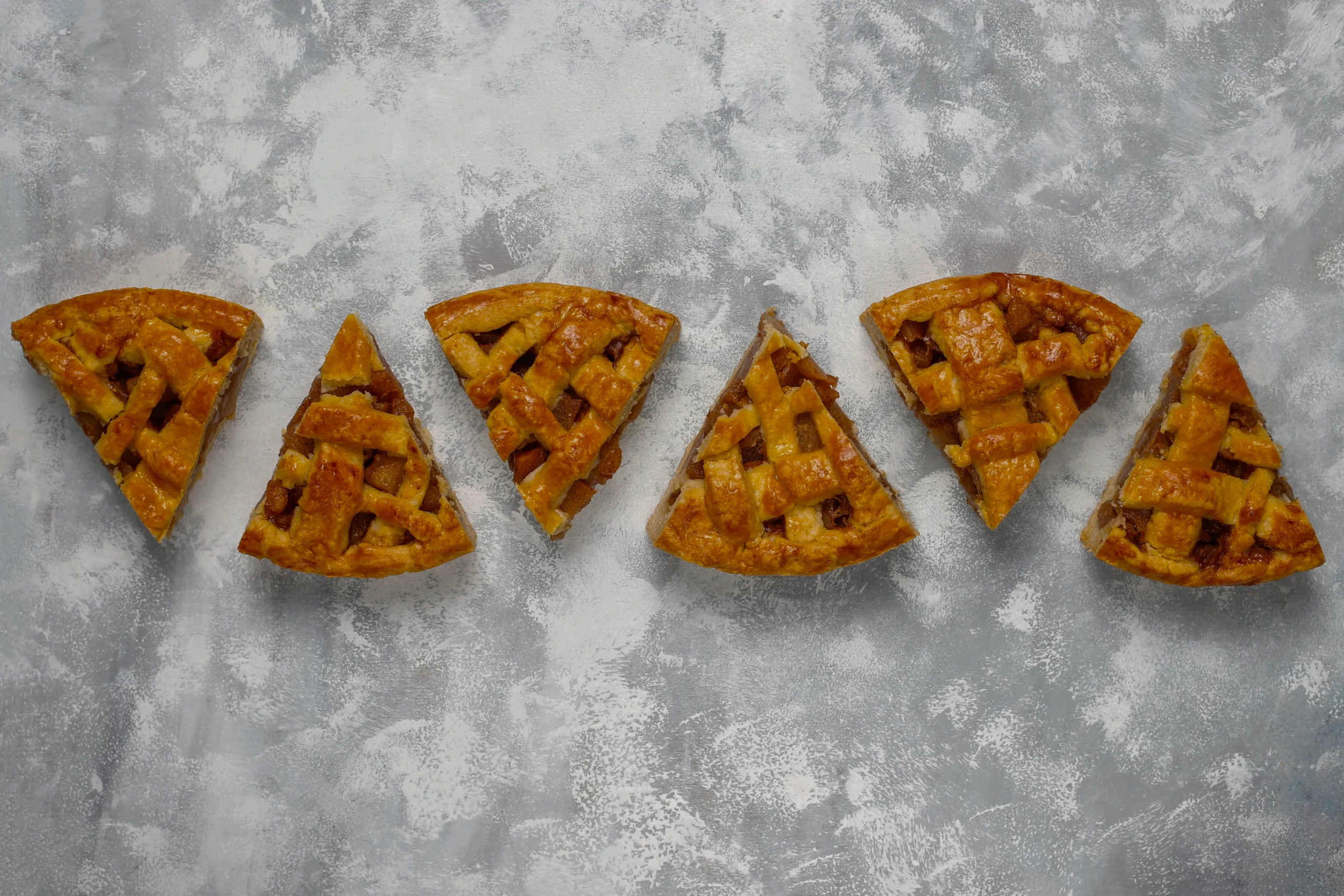 A top-down view of a rustic wooden tabletop featuring a perfectly golden-brown, flaky shortcrust tart shell. Beside the tart are a marble rolling pin dusted with flour, a small bowl of cold butter cubes, and a scattering of loose flour. Overlay text reads: "The Secret to the Perfect Crumbly Shortcrust Pastry.
