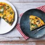 Close-up of fluffy baked eggs and sautéed seasonal vegetables in a golden-brown frittata, showing a perfect tender texture