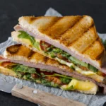 Golden brown grilled cheese sandwich cut in half, showing melted cheese and fresh tomato slices with a side of tomato soup.