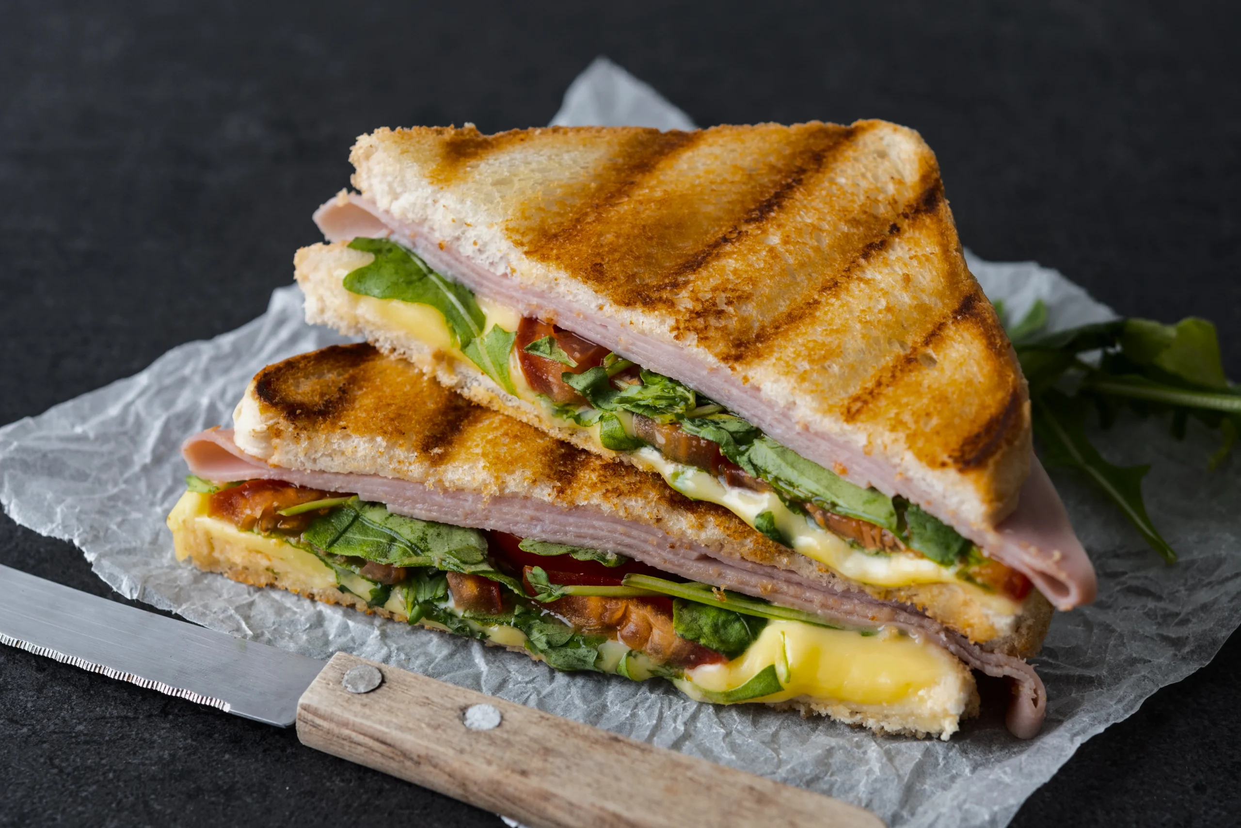 Golden brown grilled cheese sandwich cut in half, showing melted cheese and fresh tomato slices with a side of tomato soup.