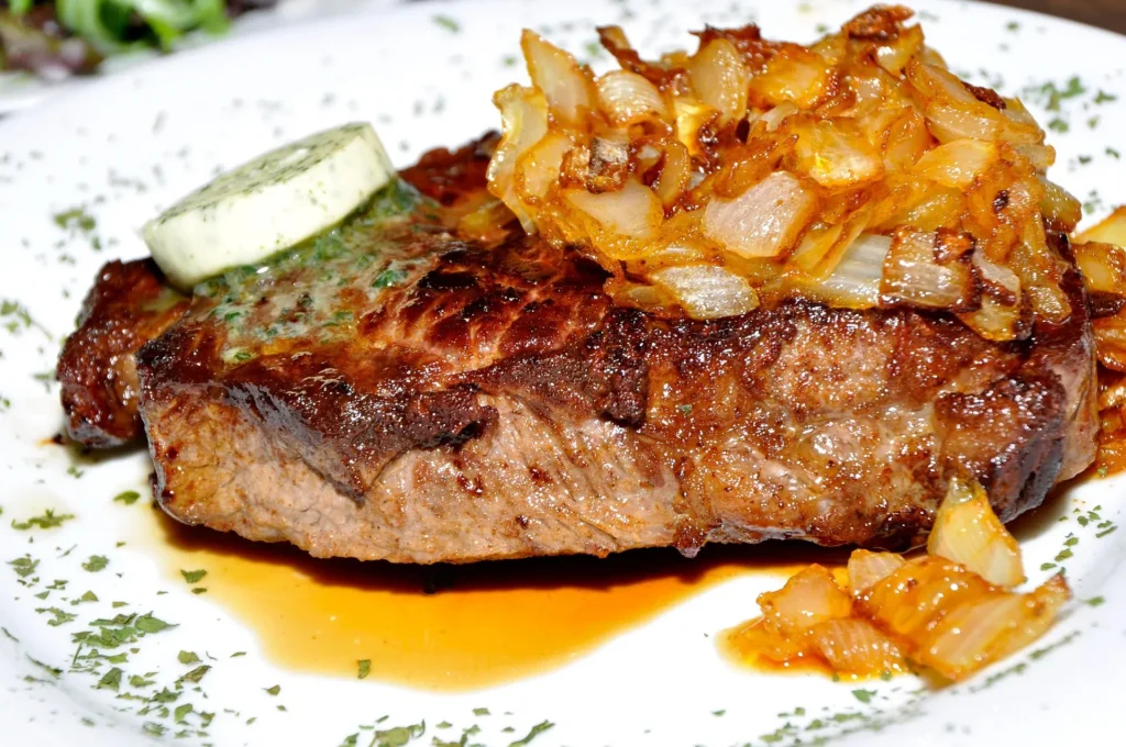 Gourmet beef steak with a glossy peppercorn sauce and fresh rosemary garnish on a dark slate platter