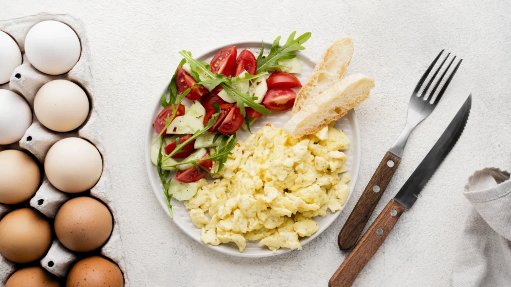 Light and airy scrambled eggs on a breakfast plate with a side of crispy bacon and roasted tomatoes.