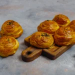 A stack of buttery puff pastry squares showing the lamination and 1-inch lift, styled with a linen napkin and a dusting of flour.