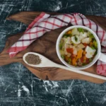 Close-up of hearty vegetable soup served in a rustic ceramic bowl with a side of crusty bread.