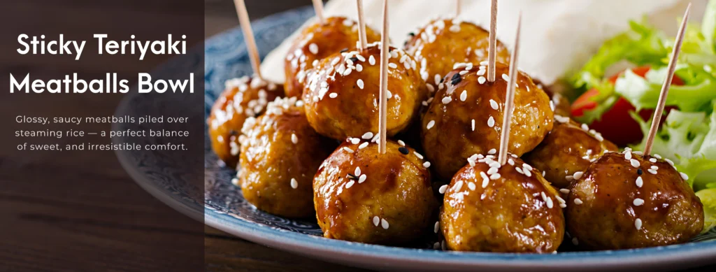 Close-up of glossy Sticky Teriyaki Meatballs over a bed of fluffy white rice, garnished with toasted sesame seeds and fresh green onions.