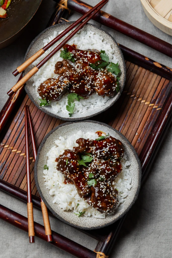 Close-up of glossy Sticky Teriyaki Meatballs with a thick dark glaze, served over a bed of fluffy white rice and garnished with sesame seeds.