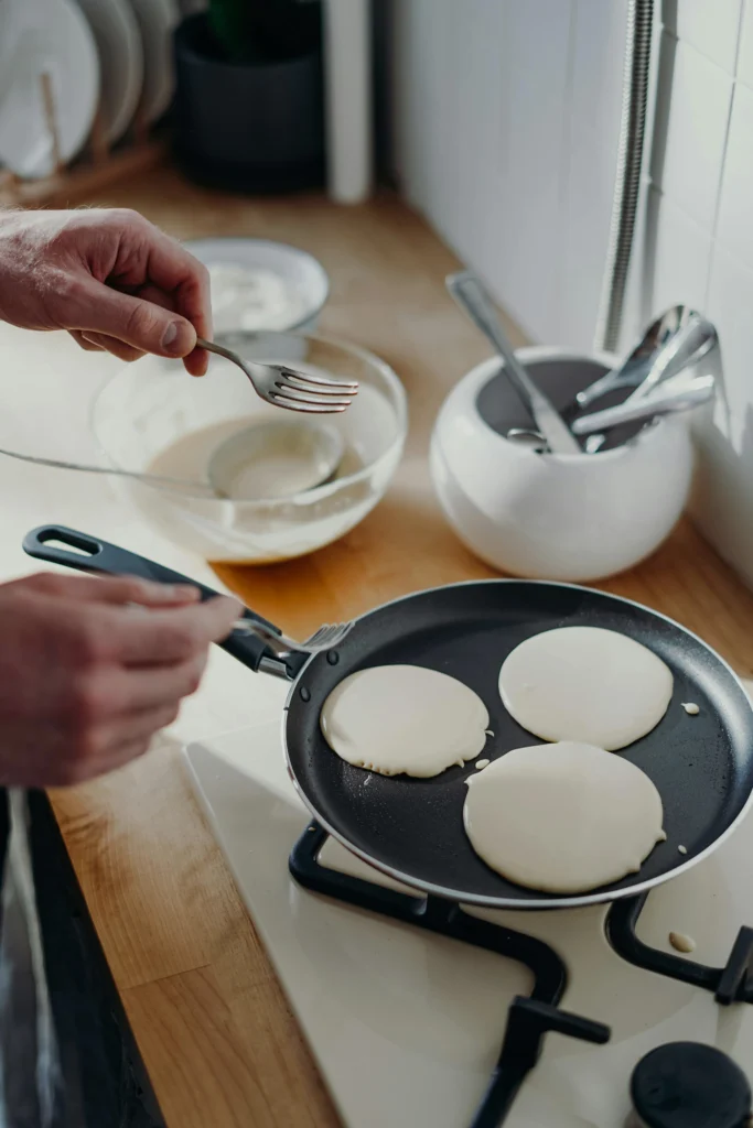 Scotch Pancakes cooking on a griddle with bubbles forming on the surface, showing perfect fluffy texture
