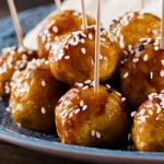 Wide-angle view of a skillet filled with Sticky Teriyaki Meatballs in a bubbling sauce, served alongside bowls of steamed jasmine rice.