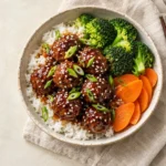 Close-up of glazed teriyaki meatballs over rice in a white bowl, ready to serve