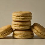 Piping honey buttercream filling between almond macaron shells before sandwiching